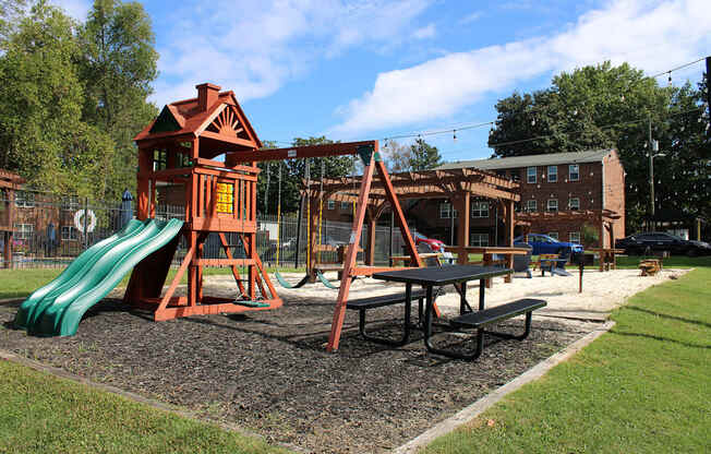 A playground with a green slide and a red wooden playhouse.