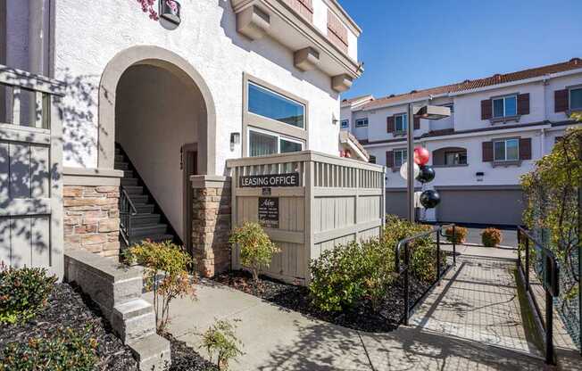 A building with a sign that says "LEASING OFFICE" is surrounded by plants and a sidewalk.