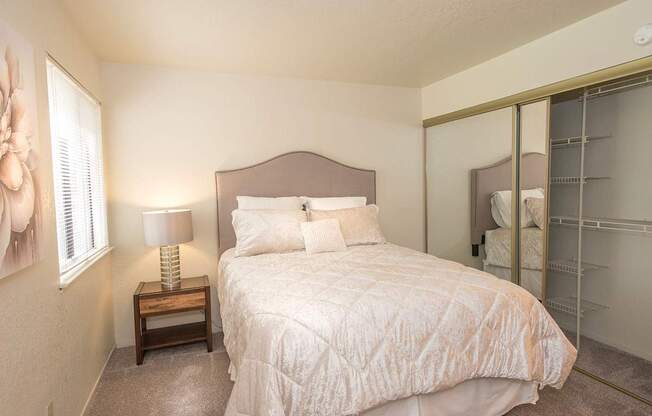 A bedroom with a bed, nightstand, and a mirror at Zinfandel Village Apartments, California, 95670