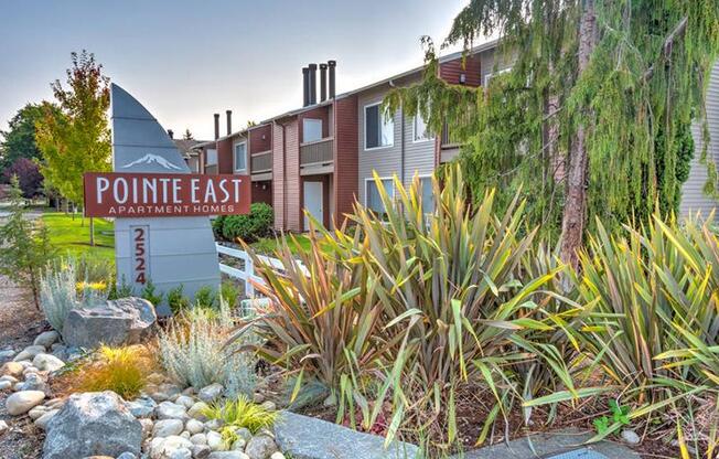 Community entrance with a Pointe East Apartment Homes sign surrounded by well-maintained landscaping with apartments in the background.
