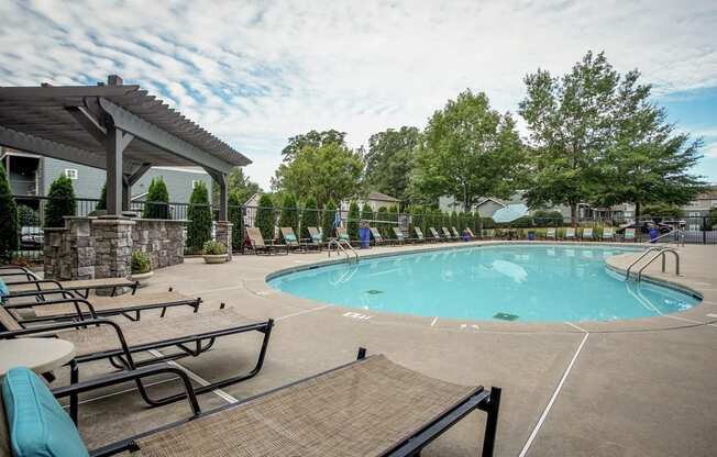 A large outdoor swimming pool surrounded by lounge chairs and trees.
