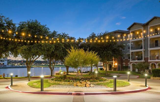 A beautifully lit garden in front of apartment buildings at dusk.