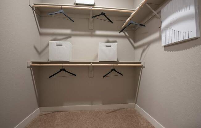 A small closet with two shelves and three hangers.