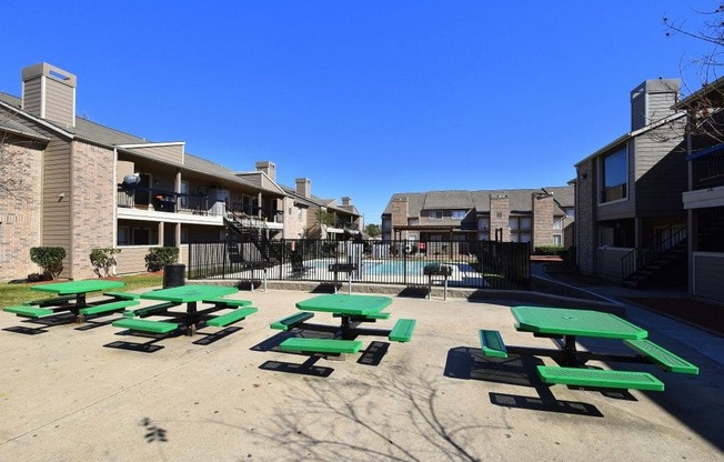 a courtyard with green picnic tables and a pool in the background