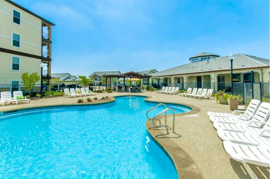 A large swimming pool surrounded by lounge chairs and buildings.