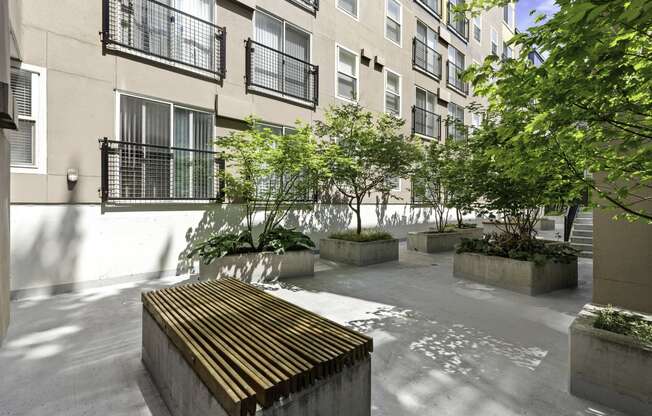 a courtyard with a wooden bench and trees in front of  Sir Gallahad Apartment Homes, Washington, 98004