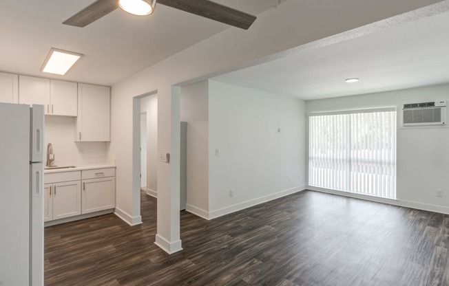 an empty living room with a kitchen in the background