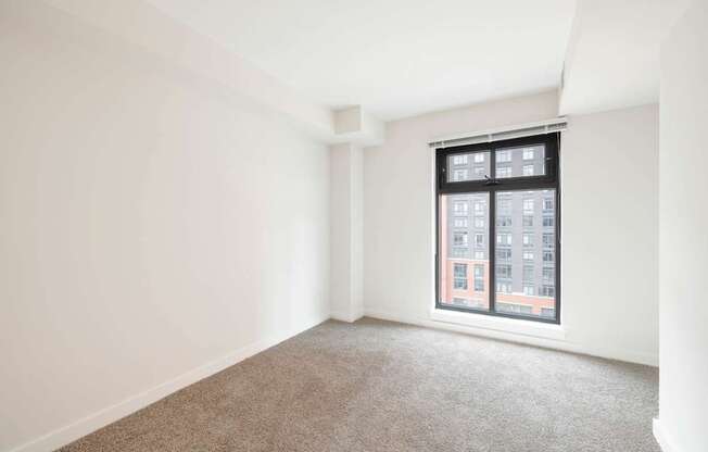 A room with a carpeted floor and a window showing a building outside.