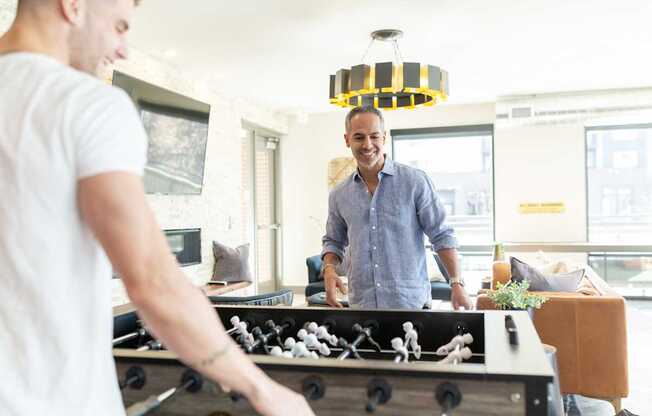 A man in a blue shirt is playing a game of foosball in a brightly lit room.