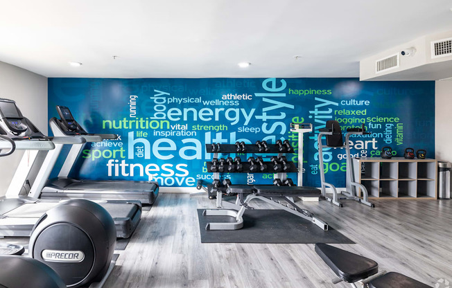 A gym with a variety of equipment and a wall with words related to fitness.