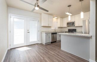 View of open kitchen with wood look flooring, stone counters, white cabinets, stainless appliances, ceiling fan, and lighting