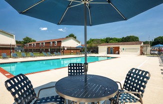 A table with chairs and an umbrella is in front of a pool.