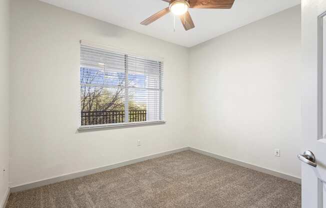 an empty room with a large window and a ceiling fan