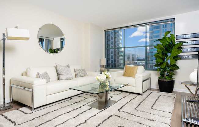 A living room with a white couch, a glass coffee table, and a mirror on the wall.