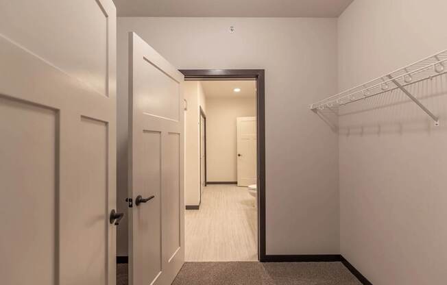 A spacious closet here at The Park featuring soft carpet, bright neutral walls, white shelving, and open doors leading to a well-lit hallway, creating a clean and functional storage space.