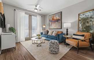 A living room with a blue couch, a patterned ottoman, and a painting on the wall.