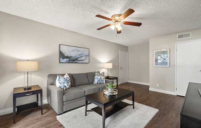 A living room with a grey couch, a coffee table, and a ceiling fan.