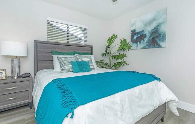 A bedroom with a bed, nightstand, lamp, and a painting on the wall.