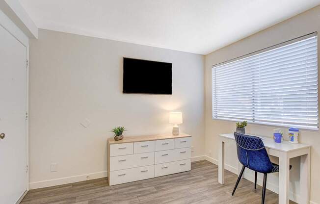 A room with a desk, chair, and a television mounted on the wall.