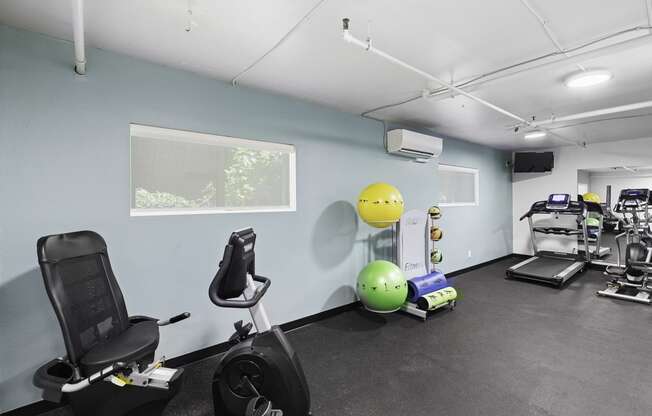 Fitness Facilities with exercise equipment like stationary bike and exercise balls with light blue walls and a window at King Arthurs Court, Seattle, WA, 98125