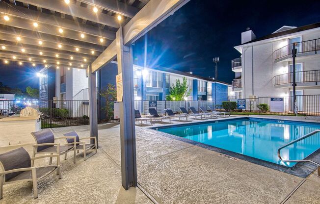 a pool is lit up at night next to a hotel pool