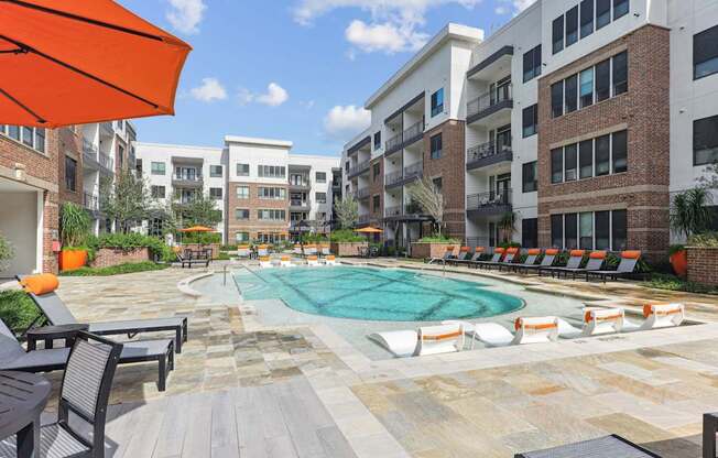 A pool surrounded by chairs and umbrellas in a courtyard.