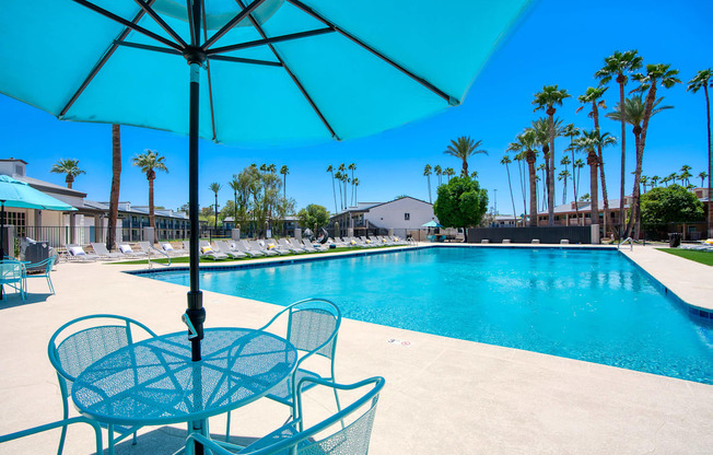 a swimming pool with tables and chairs under an umbrella at Presidio Palms Apartments, Arizona