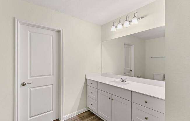 a bathroom with white cabinets, a sink and a mirror