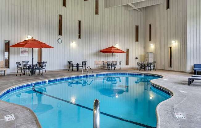 A large indoor swimming pool with a blue tinted water and a white wall in the background.