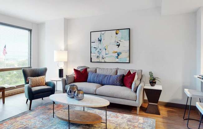 A living room with a grey couch, a black chair, a wooden coffee table, and large windows