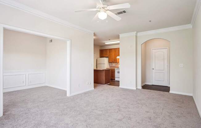 A spacious  living room with a ceiling fan and carpeted floor.