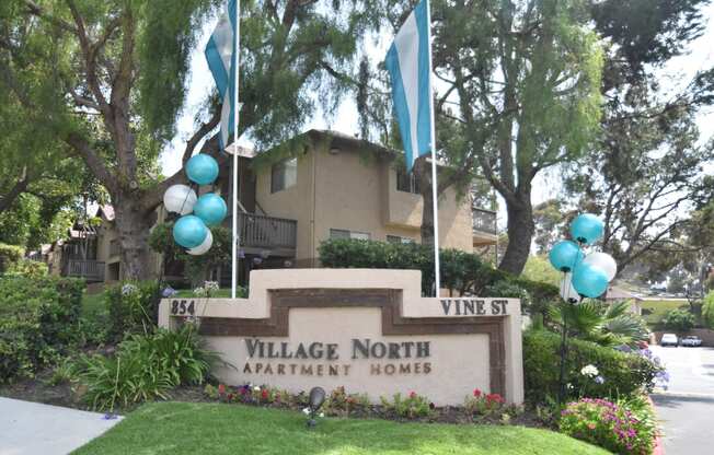 a photo of the village north apartment homes sign with blue and white balloons above it