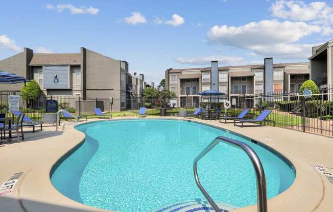 a swimming pool with lounge chairs and umbrellas with apartment buildings in the background