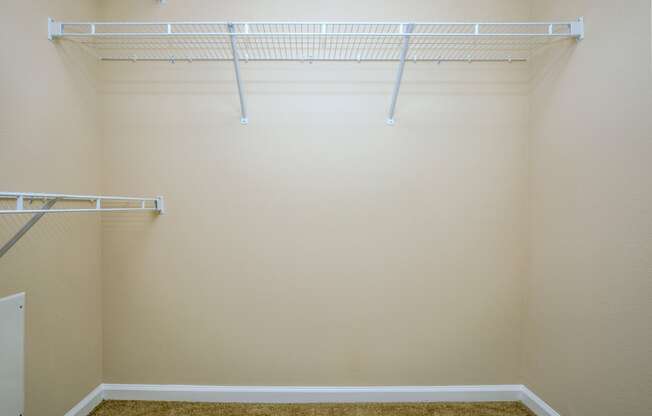 a walk in closet in an empty room with white shelves