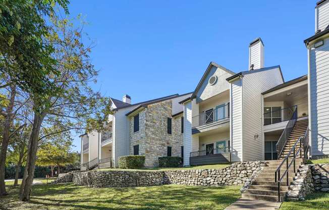 Our modern apartment buildings with a stone wall and a staircase at On the Green apartments in Austin, TX