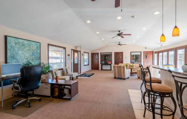 a living room with a desk and chairs and a kitchen with a table and chairs