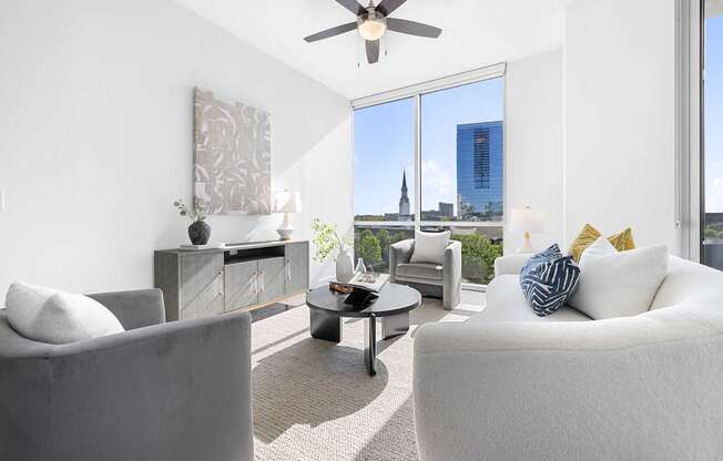 A living room with a grey couch, a white couch, a coffee table, and a ceiling fan.