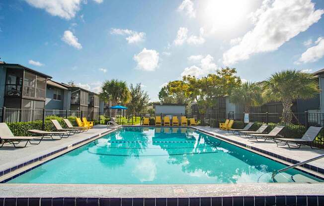 A swimming pool surrounded by sun loungers and trees.