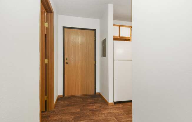 a hallway with a wooden door and a white refrigerator. Anoka, MN Dellwood Estates