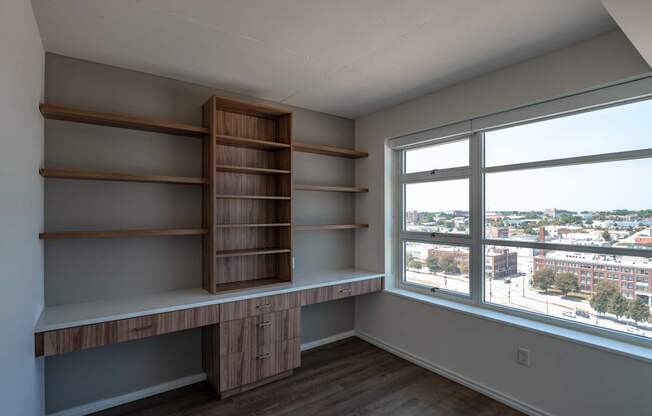 A room with a window overlooking a cityscape and a shelving unit.