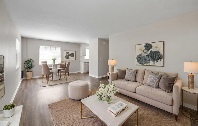 Inviting living room with cozy beige couches, elegant coffee table, and a chic dining area, offering ample natural light and modern decor.