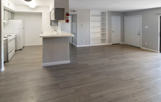 a large living room and kitchen with neutral paint and gray cabinets and white appliances and shelving