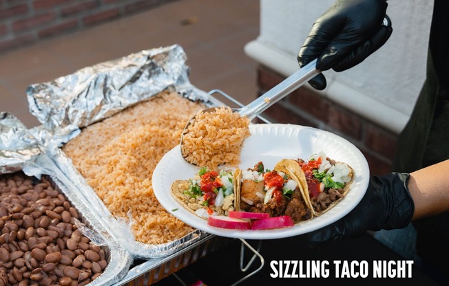 A person serving tacos at a Sizzling Taco Night event.