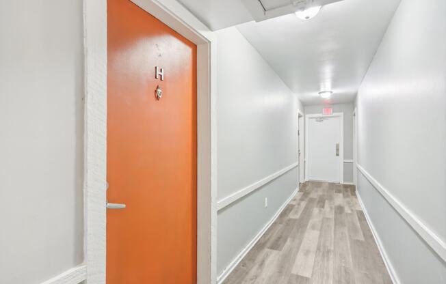 an orange door in a white hallway with white walls and wood floors