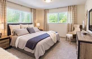 Furnished bedroom with two windows, bedside lamps, a dresser and an accent chair at Icon Avondale Apartments in Decatur, GA.