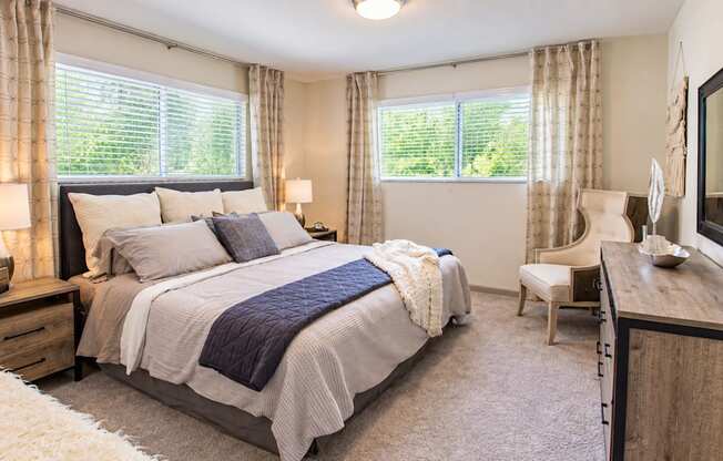 Furnished bedroom with two windows, bedside lamps, a dresser and an accent chair at Icon Avondale Apartments in Decatur, GA.