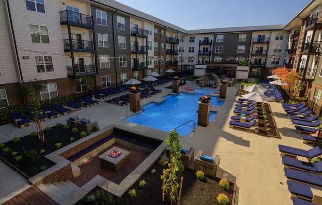 A large outdoor pool area with lounge chairs and a fire pit surrounded by apartment buildings.
