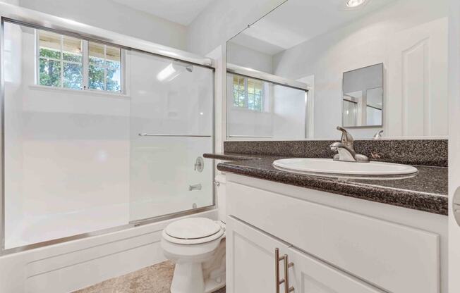 One Bedroom Apartments in San Jose CA - Los Gatos Creek - Bathroom with Small Window, Dark Countertops, and White Cabinetry