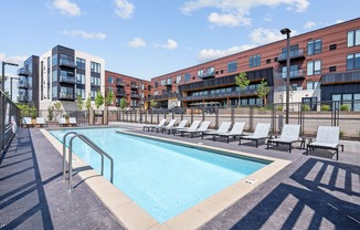 A swimming pool surrounded by lounge chairs and apartment buildings.