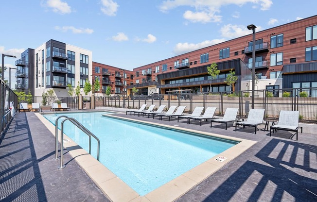 A swimming pool surrounded by lounge chairs and apartment buildings.